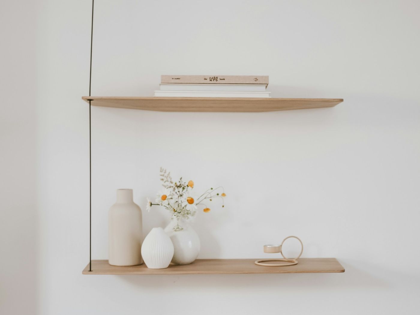 A pale wooden floating shelf holding white ceramic vases and a small bunch of dried flowers against a white wall.