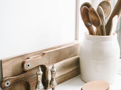 Wooden spoons standing in a white ceramic crock beside wooden cutting boards on a kitchen counter.